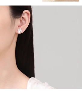 Close-up of matte silver four-petal flower stud earring worn on model's ear lobe