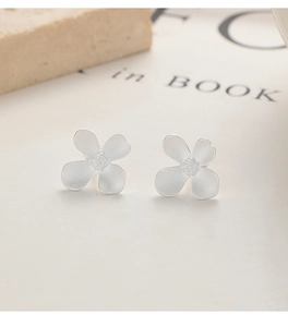 Close-up of matte silver four-petal flower stud earrings on a textured stone and book