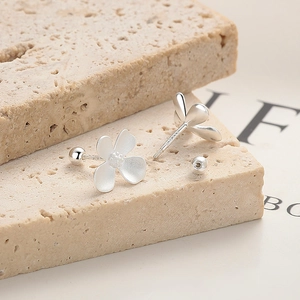 Silver 999 flower screw back earrings with matte petals on a beige stone background