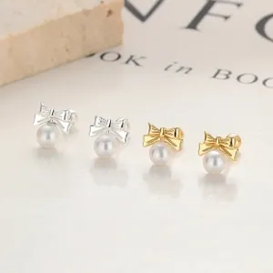 Macro detail of silver and gold bow pearl earrings on minimalist textured background