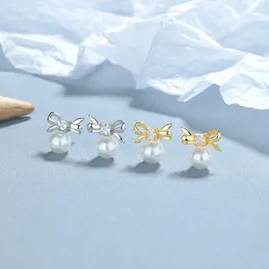 Macro view of silver and gold bow earrings with round pearls and square zircon inlays