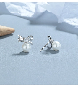 Detail of silver bow earrings with square zircon and round pearls on a textured background