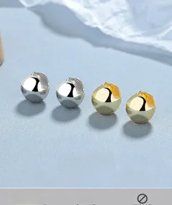 Vue détaillée de créoles sphériques polies en or et argent sur un fond bleu mat