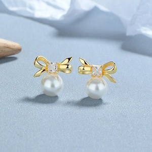 Elegant gold bow earrings with white pearl drops and shimmering zircon accents