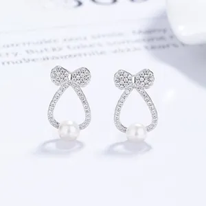 Detail of 925 silver bow stud earrings featuring micro-pave crystals and round pearls