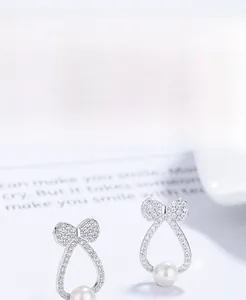 Macro shot of 925 silver bow stud earring with a round white pearl and micro-inlaid crystals