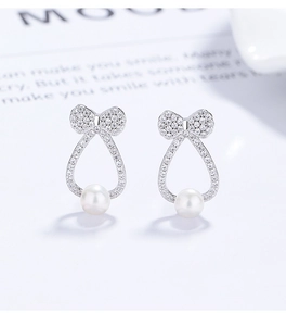 Macro detail of 925 sterling silver bow earrings featuring elegant hanging white pearls