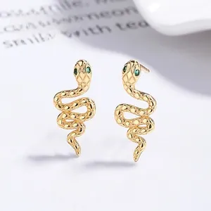 Macro detail of gold snake stud earrings with green gemstone eyes and scales
