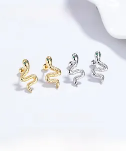 Detailed view of snake stud earrings in silver and gold with green gem eyes and screw backs