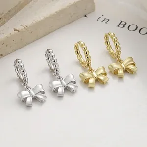 Detailed view of silver and gold ribbon bow earrings with beaded texture hoops