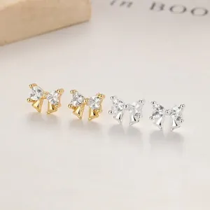 Close-up of gold and silver bow stud earrings featuring sparkling heart-shaped zircon stones