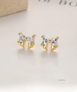 Close-up of golden bow earrings featuring heart-shaped cubic zirconia and fine plating