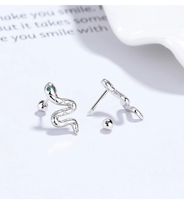 Macro detail of silver snake stud earrings with green gemstone eyes and screw-back closure