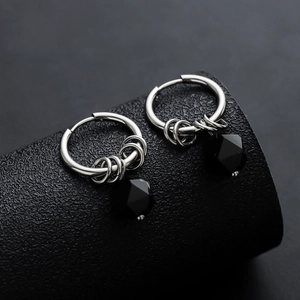 Punk style silver hoop earrings with black geometric beads on a black cylinder display