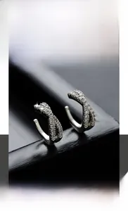 Détail macro du耳 clip croisé en acier titane avec zircons blancs étincelants