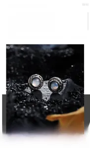 Détail de boucles d'oreilles en titane argenté avec pierre bleue sur fond de pierre noire