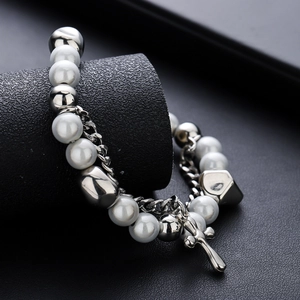 Elegant beaded cross bracelet with white pearls and silver steel accents on black pedestal