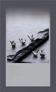 Macro detail of silver hip hop hand gesture stud earrings on black stone surface