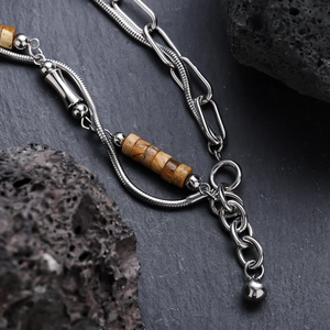 Polished silver titanium steel chain necklace with marble beads on dark stone background