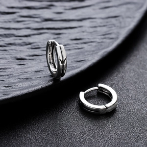 Sliver huggie earrings for men with engraved crown details on textured black background