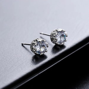 Classic round zircon stud earrings with silver crown setting on a black leather background