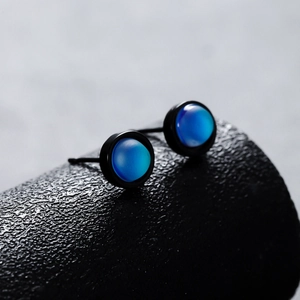 Pair of black minimalist earrings with deep blue opal inlay displayed on textured surface