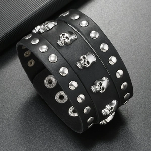Detail view of punk wide leather bracelet with silver skull charms and metal rivets