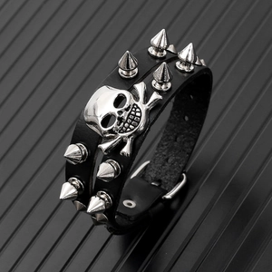 Detail of punk leather bracelet with metal spikes and skull charm on textured background