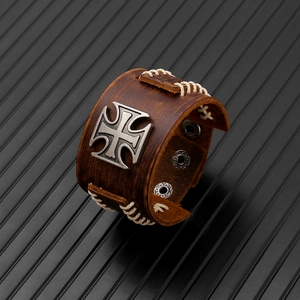 Close-up of brown leather punk bracelet with white stitching and silver iron cross badge