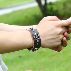 Brown leather anchor bracelet with silver metal charms worn on wrist in outdoor setting