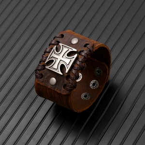 Dettagli di un bracciale in pelle punk marrone con croce d'argento e bordi intrecciati