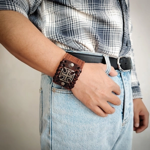 Dettaglio di bracciale punk in pelle retrò con croce in metallo incisa e cordini in pelle