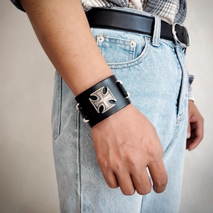Detail of wide black leather punk wristband featuring a silver iron cross and white stitching