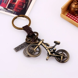 Vintage bronze bicycle keychain with brown woven leather and gear charms on white surface