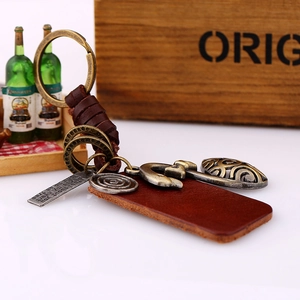 Vintage handmade leather car keychain with woven strap and retro brass charms on white table