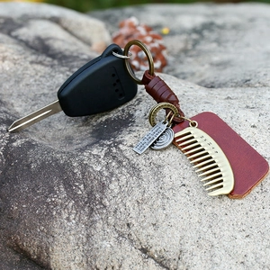 Vintage braided leather keychain with brass comb pendant and metallic nameplate on rock