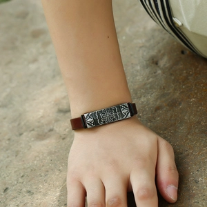 Vintage dark brown leather bracelet with embossed cross metal plate on sand stone surface