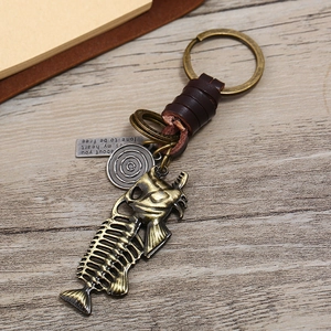 Detail of bronze fish bone pendant with leather wrap and engraved metal charms on wood