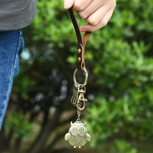 Vintage owl keychain in bronze alloy with dark brown leather strap held by a hand outdoors