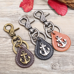 Three vintage leather anchor keychains in brown and black on grey wood background