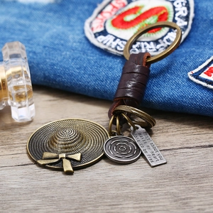 Vintage leather keychain with woven hat pendant and engraved metal plate on denim surface