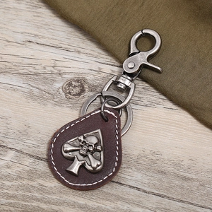 Vintage punk leather keychain with metal skull emblem on wood and fabric background