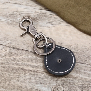Vintage black leather keychain with antique silver metal clasp on light wood background