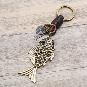 Retro handmade fish keychain with woven leather strap and bronze metal charm on wood