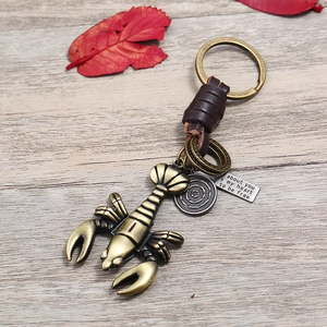 Retro bronze lobster keychain with leather wrap and engraved tag on wood background