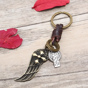 Retro handmade leather keychain with bronze alloy wings and cross charms on wood surface