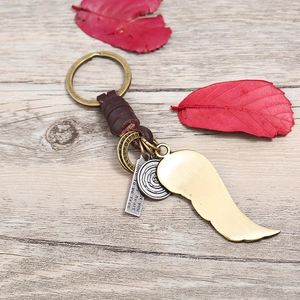 Vintage leather car keychain with brass wings and engraved metal pendants on wood