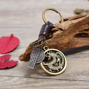 Vintage leather keychain with brass dragon charm and engraved metal tag on rustic wood