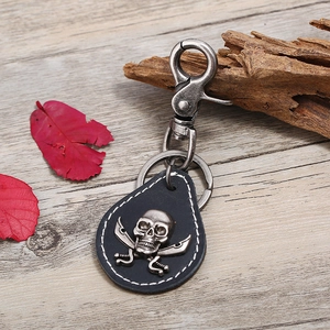 Vintage punk leather keychain with antique silver skull and crossbones on wooden background