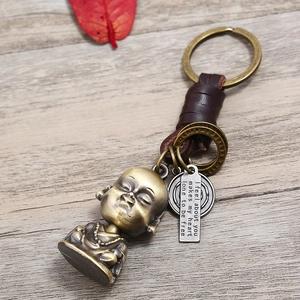 Vintage handmade leather keychain with bronze Buddha pendant and metal tag on wood